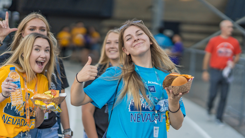 A group of students holding food and drinks give a thumbs-up to the camera during ϱFIT.