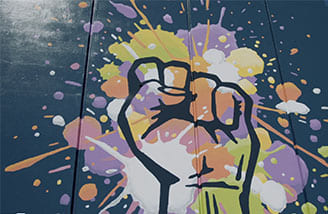 A painted mural of a hand in a fist, with splotches of pink, orange, yellow and green on the hand and surrounding portion of the mural.